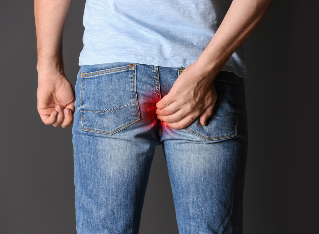 Man Suffering from Hemorrhoid on Black Background, Closeup